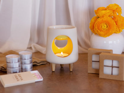 Ceramic wax warmer essential oil warmer by Arya Tara Candles. White outside yellow inside colored. Ceramic handmade tealight wax warmer with wooden legs.