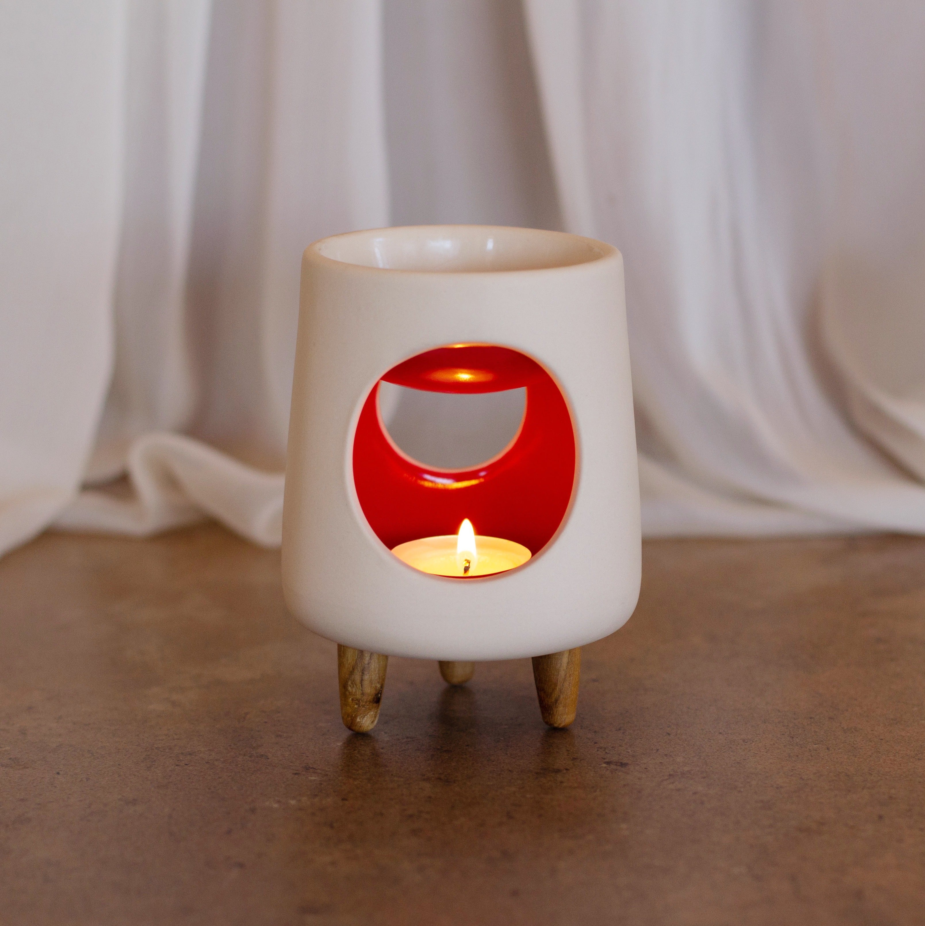 Ceramic wax warmer essential oil warmer by Arya Tara Candles. White outside red inside colored. Ceramic handmade tealight wax warmer with wooden legs.